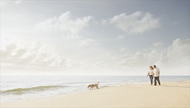 Caucasian couple walking dog on beach