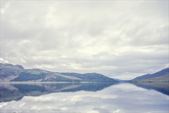 Cloudy sky and hilly landscape reflected in still lake