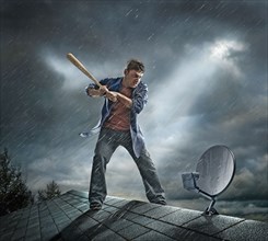 Caucasian man swinging baseball bat at satellite dish on roof