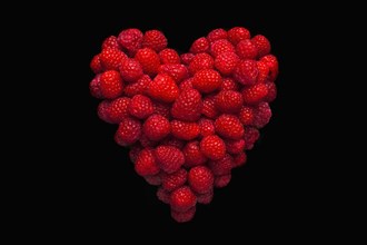 Raspberries in shape of heart on black background