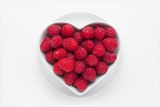 Raspberries in heart-shape bowl on white background