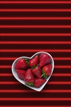 Strawberries in heart-shape bowl on red striped background