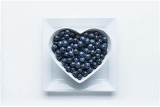 Blueberries in heart-shape bowl on white background