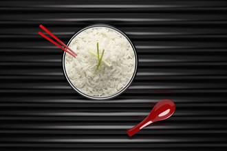 Chopsticks in bowl of white rice with red spoon