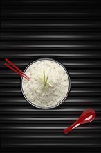 Chopsticks in bowl of white rice with red spoon