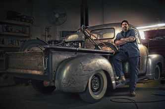 Caucasian mechanic posing on vintage truck with motorcycle