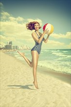 Caucasian woman running on beach carrying beach ball