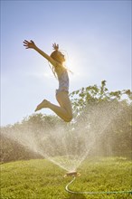 Caucasian girl jumping over backyard sprinkler