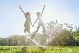 Caucasian girls jumping over backyard sprinkler