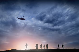 Silhouette of helicopter flying over people at sunset