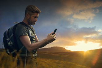Caucasian hiker texting on cell phone at sunset