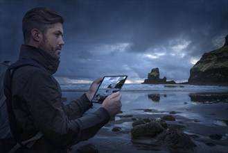 Caucasian hiker photographing beach with digital tablet at sunset