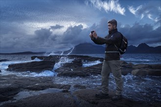 Caucasian hiker photographing ocean with cell phone