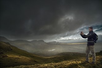 Caucasian hiker photographing storm clouds over landscape