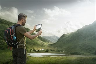 Caucasian hiker photographing valley lake with digital tablet