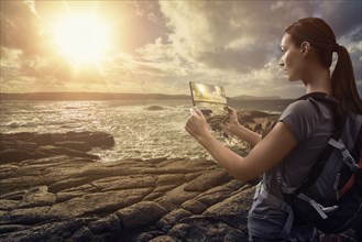 Caucasian woman photographing ocean sunset with digital tablet