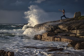 Distant Caucasian woman doing yoga on rocks near ocean