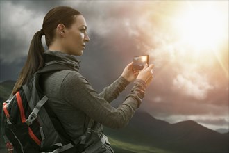 Caucasian woman photographing mountain landscape with cell phone