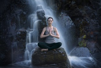 Caucasian woman meditating on rock near waterfall