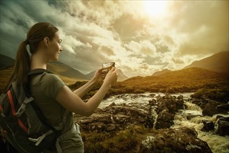 Caucasian woman photographing mountain river with cell phone