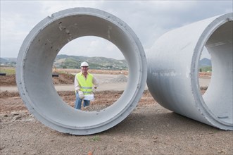 Hispanic worker standing near large cement pipes