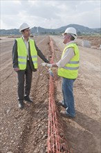 Hispanic businessman and construction worker standing in field