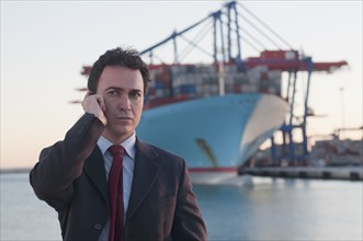 Hispanic businessman talking on cell phone with container ship in background