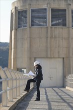 Female engineer looking at technical drawing outside hydro electric power station side view
