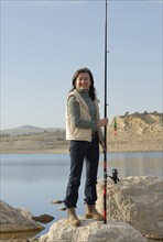 Mature woman at lakeside holding fishing rod smiling portrait