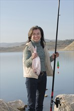 Mature woman at lakeside holding fishing rod and fish smiling portrait