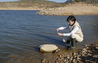 Female scientist taking water sample from lake side view