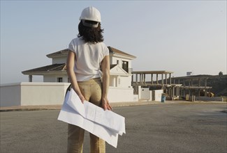 Female architect with plan looking at house in new development
