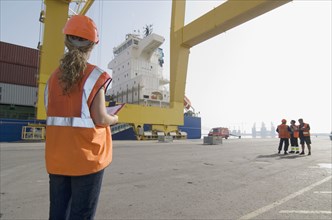 Woman wearing hard hat holding clipboard standing on dockside