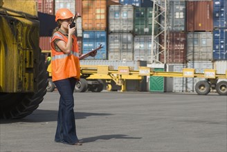 Woman wearing hard hat using walkie-talkie at container terminal