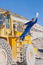 worker waving hard hat climbing mining machine