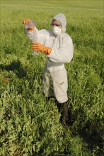 Woman in boiler suit standing in field pouring liquid into test tube
