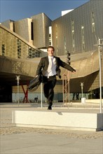 Businessman jumping bench in front of modern office building