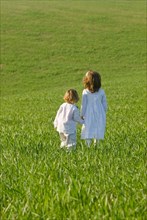 Young brother and sister holding hands in field rear view
