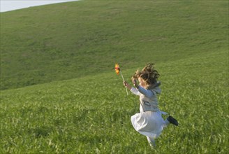 young girl with wind wheel running in green fields