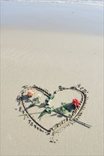 Roses laid on heart drawn in sand