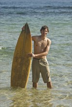 Young surfer standing in water holding surfboard portrait