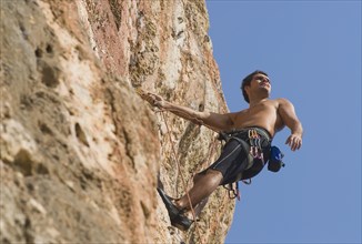 Male rock climber scaling rock face secured by ropes low angle view