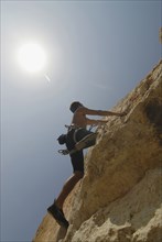 Male rock climber scaling rock face secured by ropes low angle view