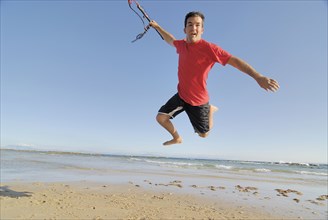 Male kite surfer jumping on beach