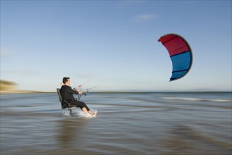 Businessman on chair pulled by surfing kite in sea
