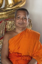 Thai Buddhist monk smiling near statue