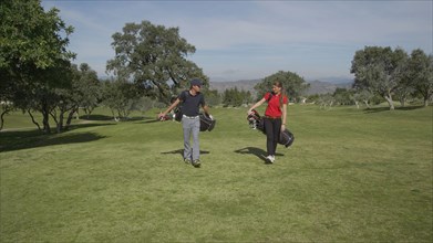 Caucasian couple carrying golf bags on course