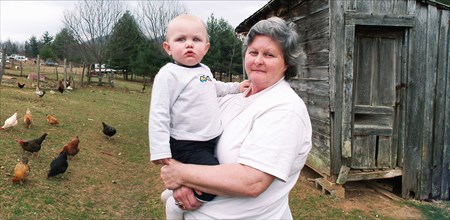 Grandmother carrying grandson near chicken coop on farm