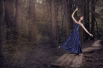 Caucasian woman wearing blue gown dancing in forest