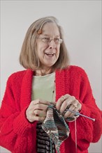 Caucasian woman wearing red sweater smiling and knitting